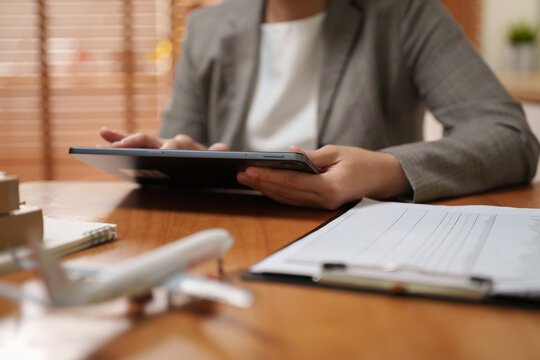 Asian Businesswoman using a digital tablet at a desk with logistics documents and airplane model, representing air freight, cargo shipping, transport planning and supply chain management.