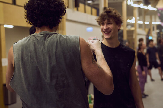 Two diverse young friends sharing a fist bump and laughter in a lively indoor gym or studio setting