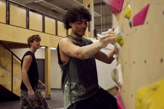 Young diverse men bouldering together on an indoor climbing wall training strength and technique