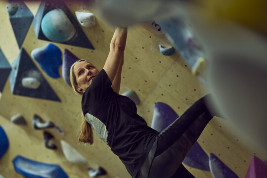 Woman bouldering on an indoor climbing wall showing strength, focus and technique during training session