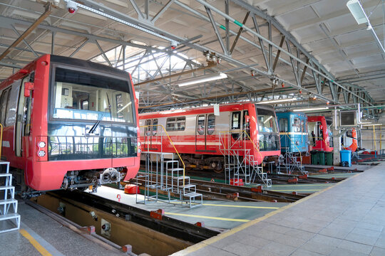 Subway trains sit in a maintenance depot for repairs and inspections during the bright daytime in a large indoor industrial facility