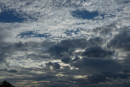 Blue Stormy Sky with Dramatic Layered Clouds and Sunlight. Blue-toned sky covered with dramatic layers of dense clouds, with brighter sunlight filtering through openings in the cloud cover. A natural 