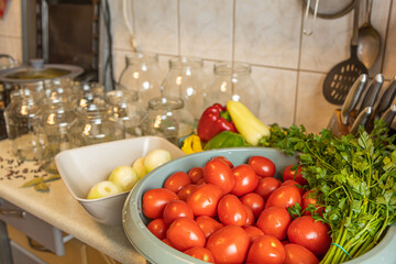 Fresh Tomatoes and Parsley Prepared for Homemade Canning With Seasoned Glass Jars. A basin filled with fresh ripe tomatoes and green parsley stands in the foreground, while transparent glass jars  © Nadiia
