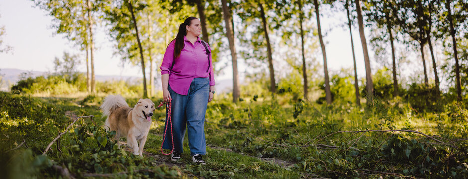 Woman Walking Her Dog Through a Sunny Woodland Park Trail in Casual Clothing for Leisure