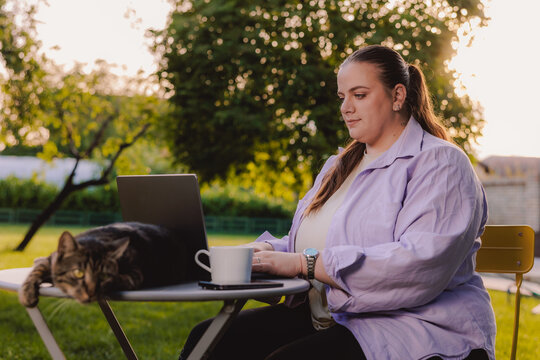 Woman Working Remotely on Laptop in Garden With Cat and Coffee During Sunset
