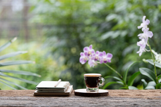 Coffee and notebooks and pencil on wooden table with purple orchid background