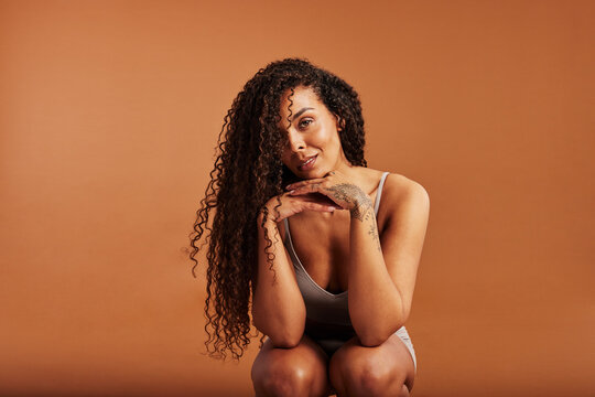 Smiling black woman crouching in underwear against an orange background