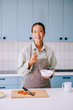 Smiling Woman Cooking in Modern Home Kitchen Wearing Apron While Preparing Fresh Tomatoes