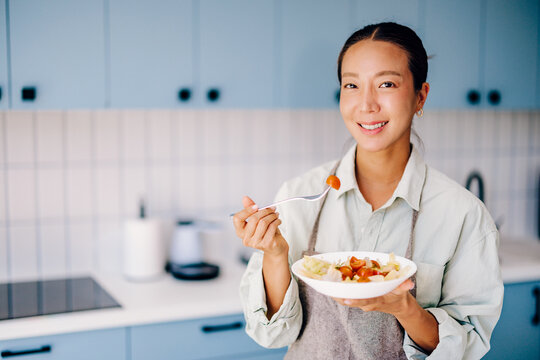 Smiling Young Woman Eating Salad in Bright Home Kitchen Enjoying Healthy Eating and Home Cooking