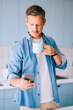 Man Checking Phone While Drinking Coffee In Modern Kitchen &mdash; Casual Morning Remote Work Lifestyle