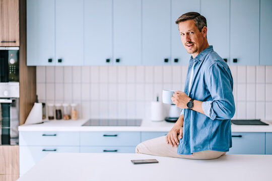 Casual Man Drinking Coffee in Modern Kitchen While Working From Home and Smiling at Camera