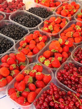 Assorted fresh berries in plastic containers at farmers market - raspberries, blackcurrants and blueberries for sale