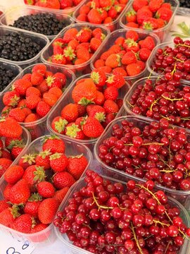 Assorted fresh berries in plastic containers at farmers market - raspberries, blackcurrants and blueberries for sale