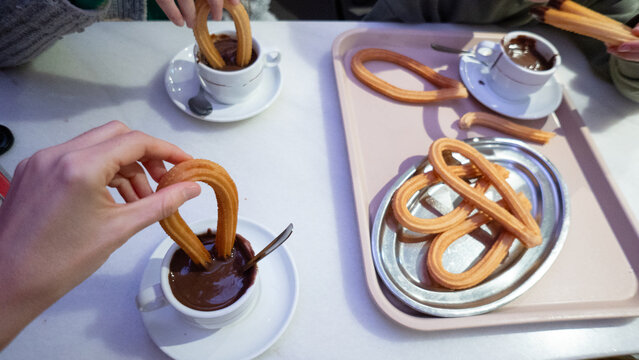 People dipping churros in rich hot chocolate sauce