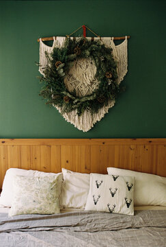 A bed with a wooden headboard beneath a macrame and evergreen wreath.