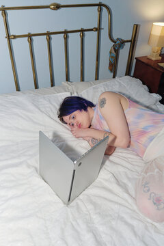 Non-binary person resting in bed looking at their computer