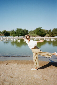 Woman balancing on one leg near a lake with flamingos.