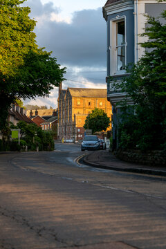 A quiet road leads into Mistley village, Essex, with historic buildings glowing in evening sunlight beneath dramatic clouds. Ideal for travel, heritage, architecture, and English countryside themes.