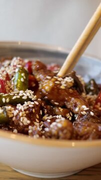 Delicious bowl of asian cuisine featuring teriyaki beef, sesame seeds, and chili peppers being eaten with wooden chopsticks, showcasing a savory and spicy meal from a restaurant menu
