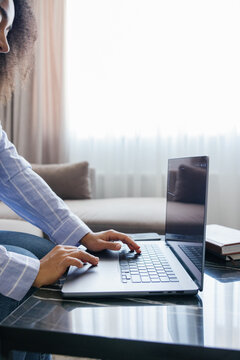 Cropped black woman typing laptop computer at desk at blurred home