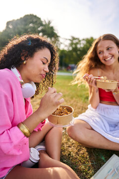 Young women friends enjoying outdoor eating in park