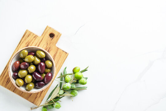 Olives in wooden bowl and fresh olive tree branch at white background.
