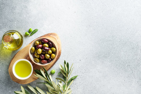 Olives in wooden bowl and fresh olive tree branch at white background.