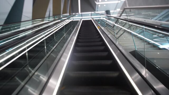 POV ascends on an illuminated escalator inside a modern transit station toward a brightly lit concourse