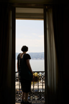 Woman Stands by Balcony Looking at Lake View