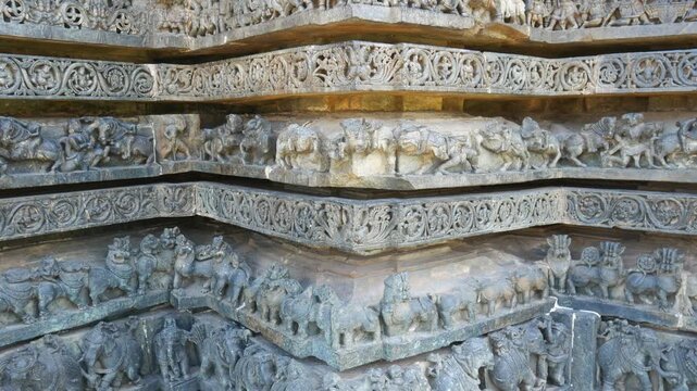 PAN: Intricately carved stone relief at the historic Hoysaleswara Temple in Halebidu, Karnataka, India, depicting richly ornamented Hindu deities and figures in detailed Hoysala architecture