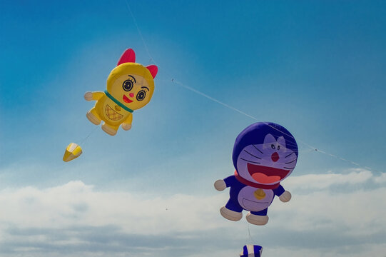 Surabaya, Indonesia - August 30: Giant Doraemon and Dorami shaped kites fly across the sunny blue sky during the annual outdoor kite festival event, Indonesia, 30 August 2026