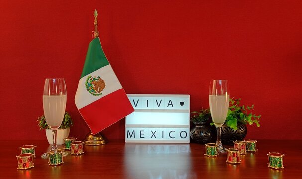 Viva Mexico Independence Day Celebration with Mexican Flag and Festive Drinks. Patriotic still life featuring the Mexican flag, festive drinks, colorful miniature drums, plants and a lightbox reading 