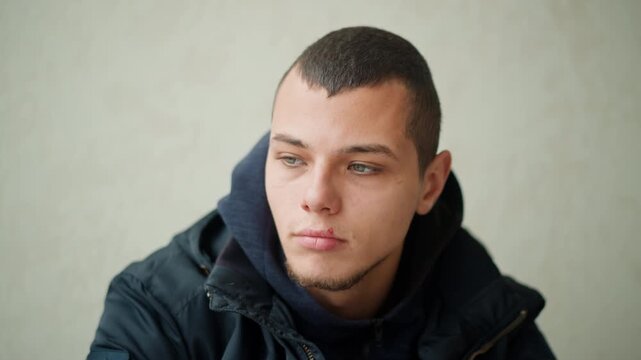 Close up of young man wearing dark clothing against plain background. Subject remains still with minimal movement maintaining consistent expression and posture. Soft lighting creates even