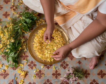 Yellow senna flowers being arranged into a ring on a hammered brass plate, featuring soft and organic textures for traditional craft and floral art