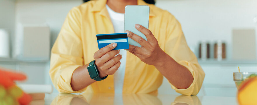 Focused Young Woman With Smartphone In Hand And Credit Card Attentively Shopping Online In Modern Office Environment. Business Concept Emphasizing Digital Payments And Online Shopping Experiences.