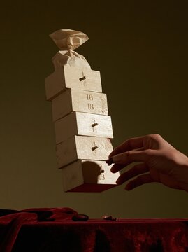 Advent calendar drawers levitating in a precarious stack above a velvet surface, featuring weathered wood and a soft paper bag for festive seasonal advertising