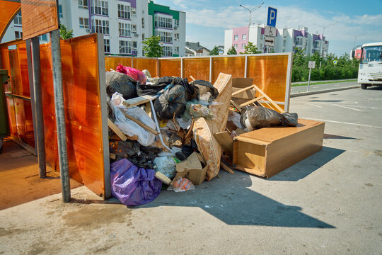 Spring mattress leaning against overfilled plastic trash bags at an unofficial waste collection site in a residential area
