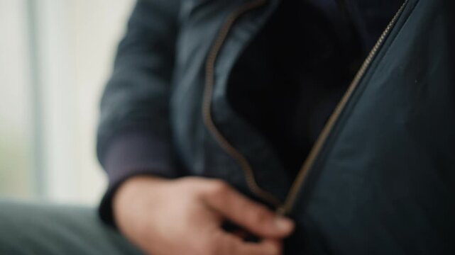 Close up of person hands unzipping front pocket on their dark jacket revealing empty interior. focus remains solely on hand movement and zipper interaction throughout sequence. Soft natural
