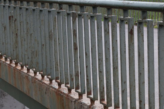 Close-up of aged metal railing with vertical bars and rusted base on a bridge