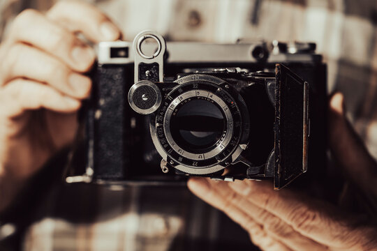Closeup of hands holding vintage folding camera. Man holding antique classic film camera with bellows detailed retro photography equipment and hobby concept backdrop