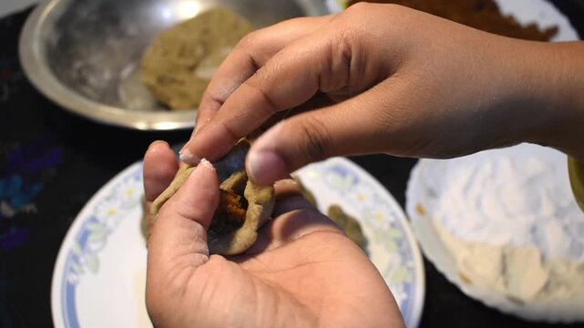 Hands filling coconut and jaggery stuffing into flour dough while preparing traditional steamed modak, or ukadiche modak, for Ganesh Chaturthi.