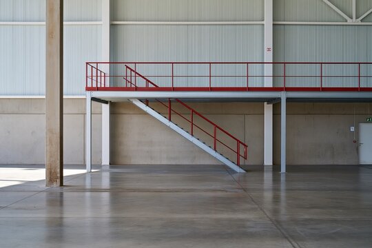 Empty industrial warehouse with a steel mezzanine and red railings, featuring polished concrete floors for logistics and real estate backgrounds