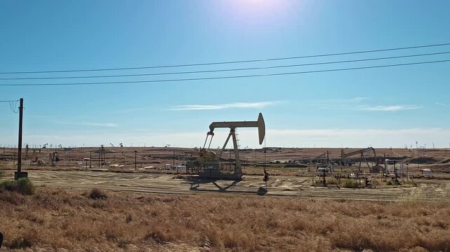 Oil pumpjacks operate across an arid field in Kern County California, Industrial energy footage shows petroleum machinery beneath a clear blue sky