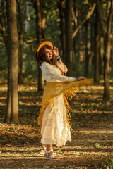 A young woman strolls calmly and casually through a field  she is wearing an open yellow shawl and a brown hat, with her arms spread wide. Boho style. © Светлана 