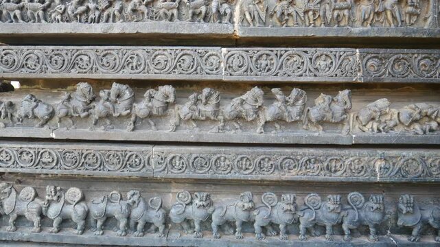 PAN: Intricately carved stone relief at the historic Hoysaleswara Temple in Halebidu, Karnataka, India, depicting richly ornamented Hindu deities and figures in detailed Hoysala architecture