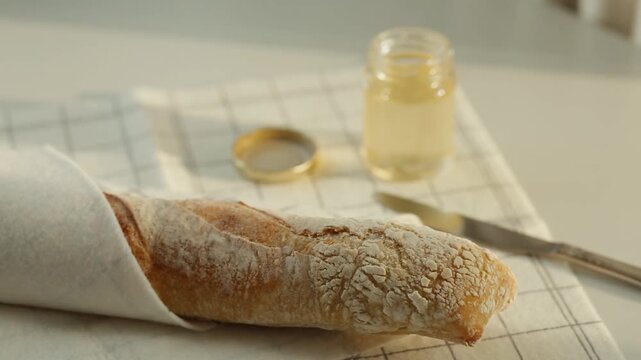 White bread wrapped in a towel and a jar of acacia honey and а kitchen knife. Concept of bakery.