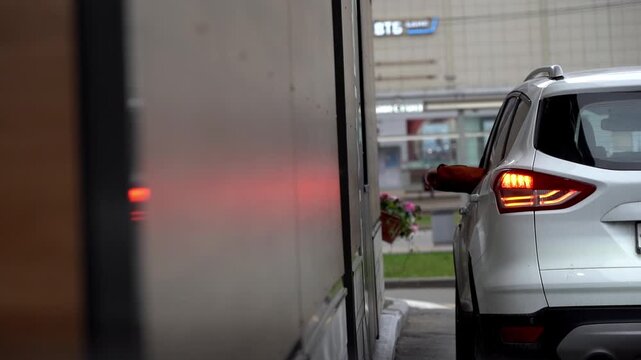 White SUV parked beside a truck. Driver signals with hand from car window. Red taillights glow softly in dim light. Urban parking scenario captured candidly. Good for business, transit