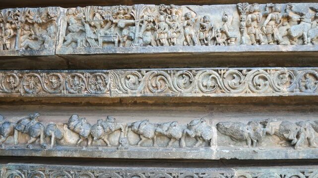 PAN: Intricately carved stone relief at the historic Hoysaleswara Temple in Halebidu, Karnataka, India, depicting richly ornamented Hindu deities and figures in detailed Hoysala architecture