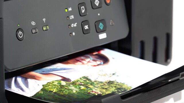 Colorful print emerges from printer tray. Young woman smiles through green foliage image. Printer displays active status lights and buttons. Ideal for home, office, or tech print promotion