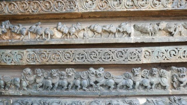 PAN: Intricately carved stone relief at the historic Hoysaleswara Temple in Halebidu, Karnataka, India, depicting richly ornamented Hindu deities and figures in detailed Hoysala architecture